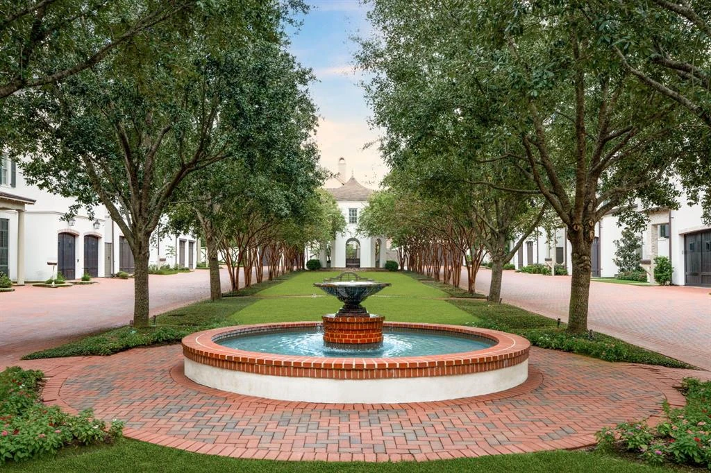 Tree-lined courtyard with a circular fountain, lawn, brick paths, and surrounding homes.