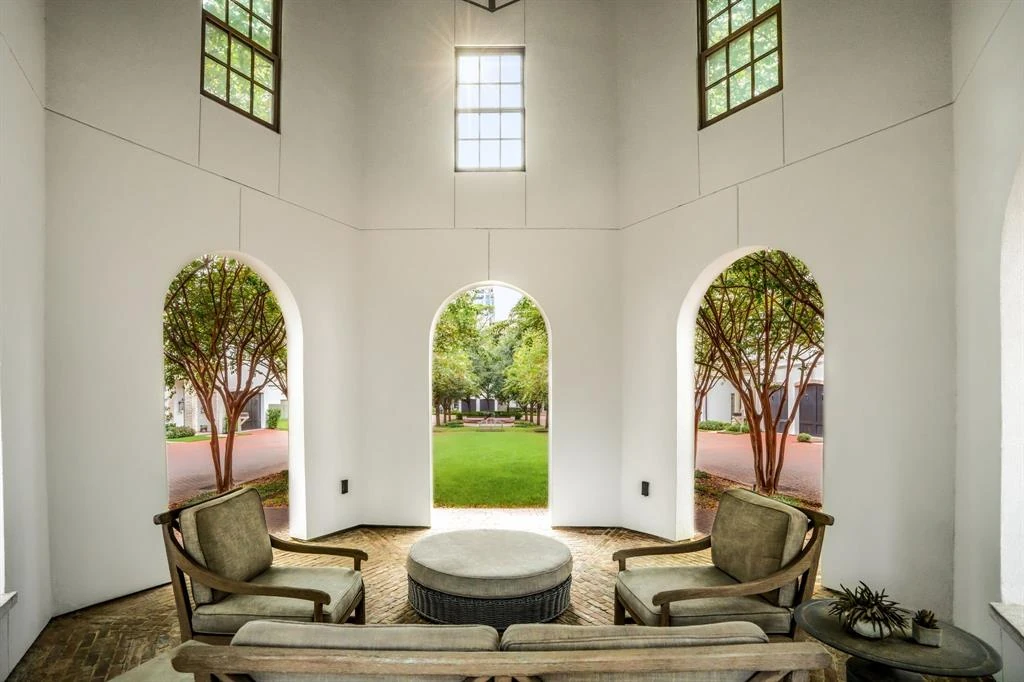 Covered seating area with chairs and a sofa beneath tall arched openings overlooking a courtyard.