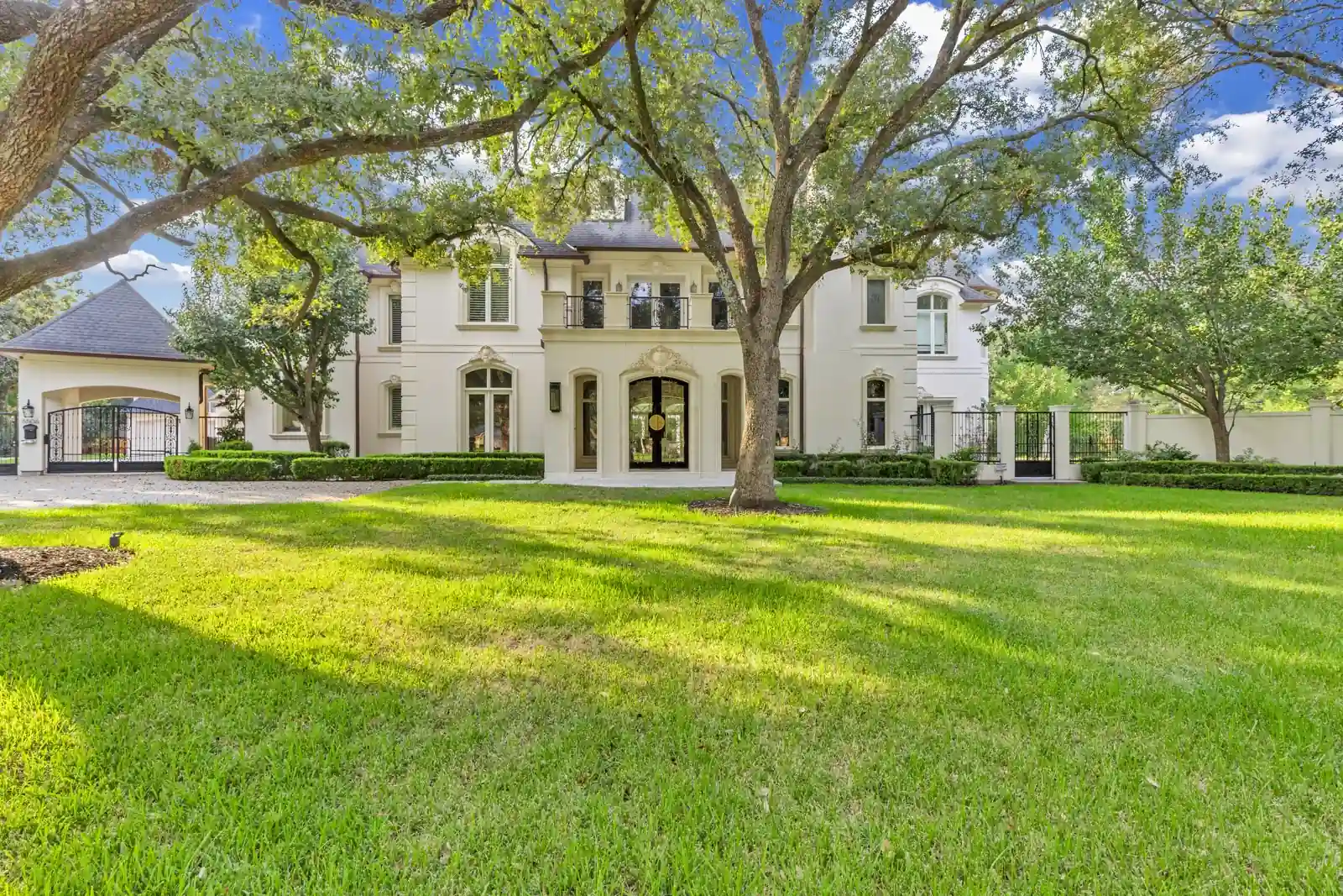 Two-story cream-colored home with an arched entrance, lawn, and mature trees.